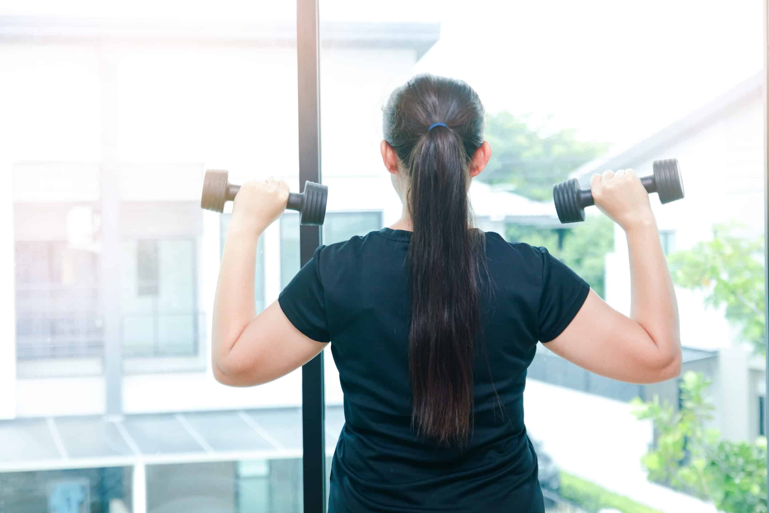 Woman lifts weights while looking out window, hoping to tone up the loose skin on her arms