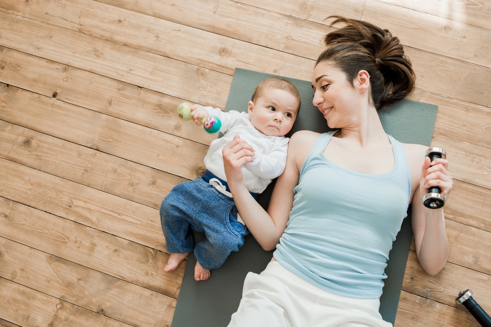 Young mother lies on the floor beside her baby trying to keep a fit postpartum body.