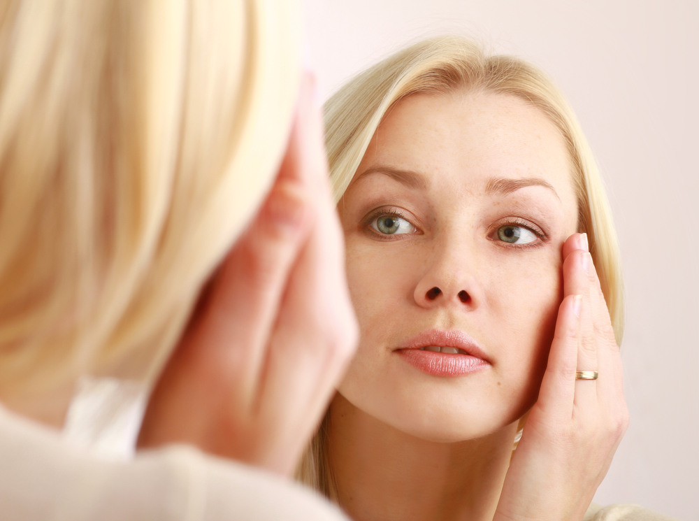 Woman examines her pretty face in the mirror.
