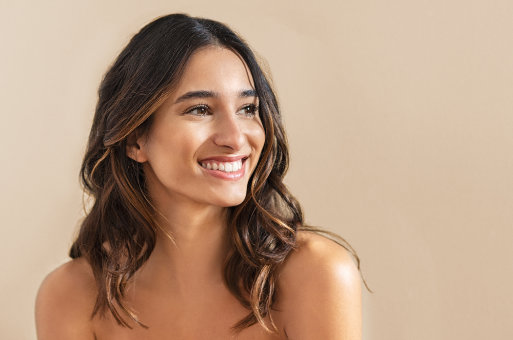 Woman in a pink lace top looking to the side against a warm beige background.